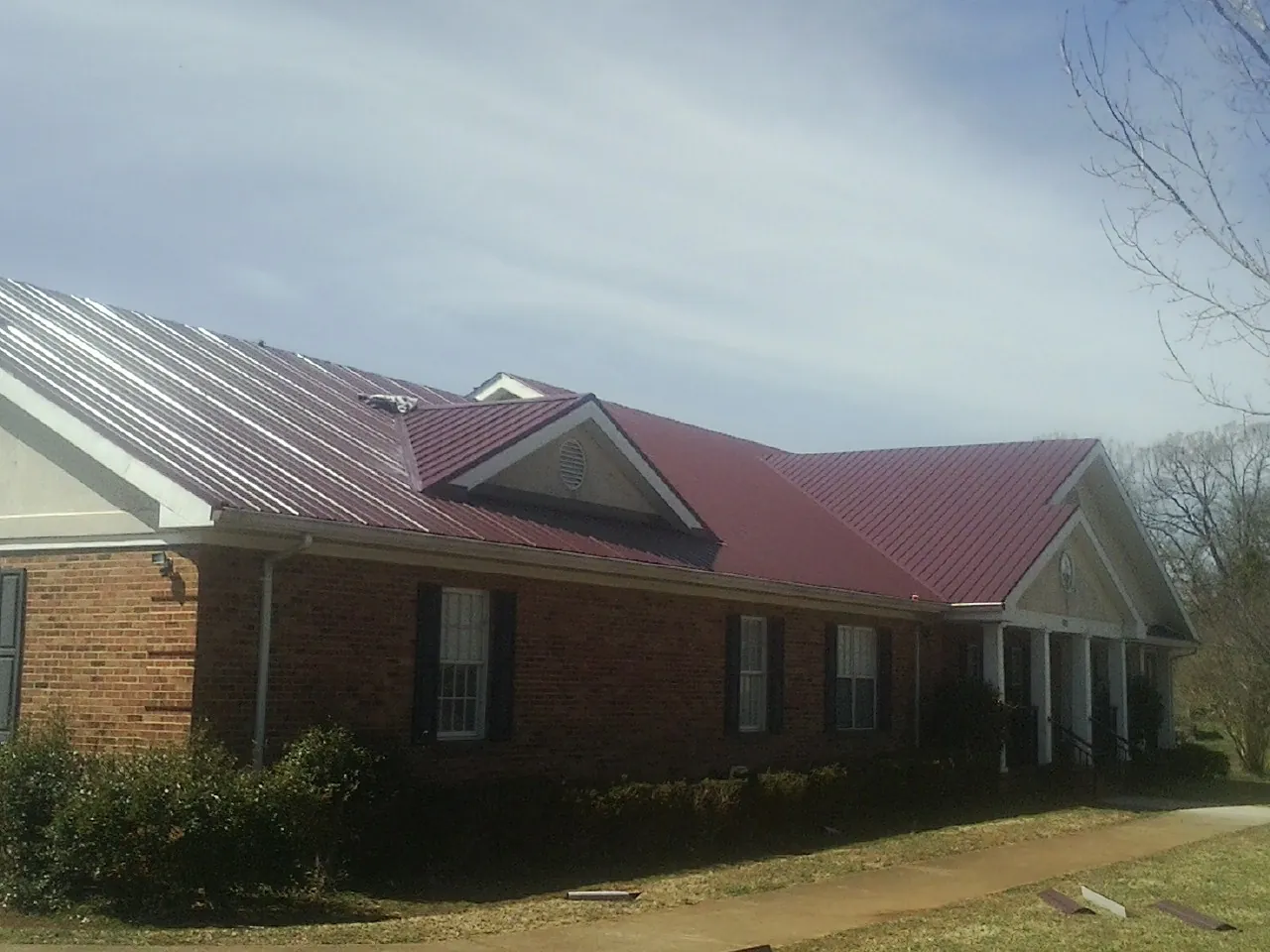Red metal roof with gabled entries on a long brick building, from a Hail Damage Roof Repair job in Hillsdale