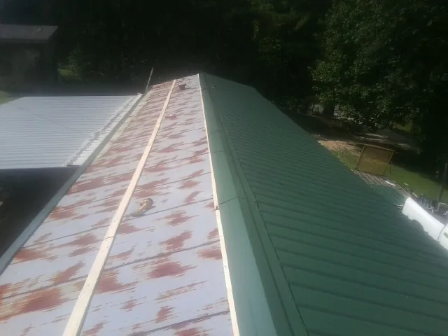 Old rusted panels beside newly installed green metal roofing — Wind Damage Roof Repair by Roofing Brothers in Hillsdale