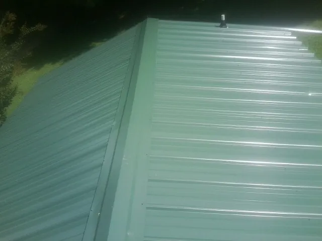 New green metal panels meeting at the ridge of a roof — Flat Roof Repair work by our crew in Hillsdale