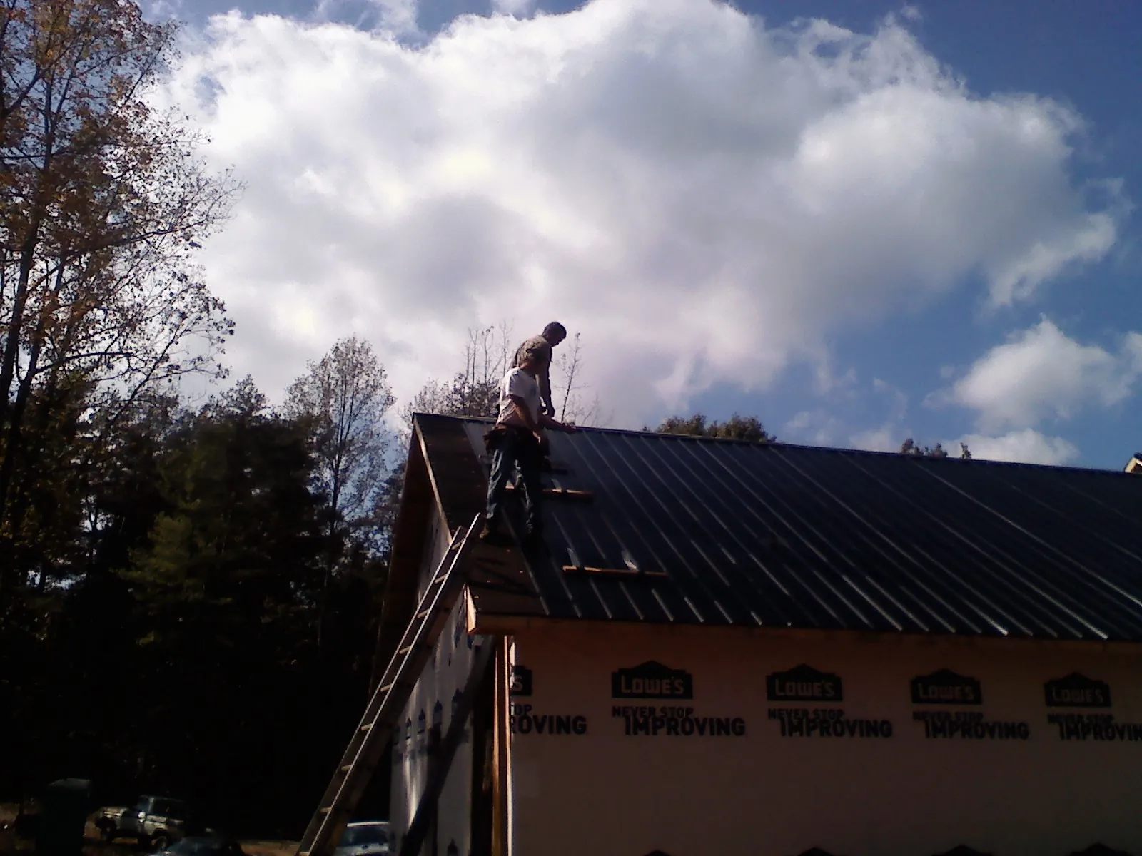 Roofer fastening dark metal panels high against a cloudy sky, from a Roof Inspection job in Hillsdale